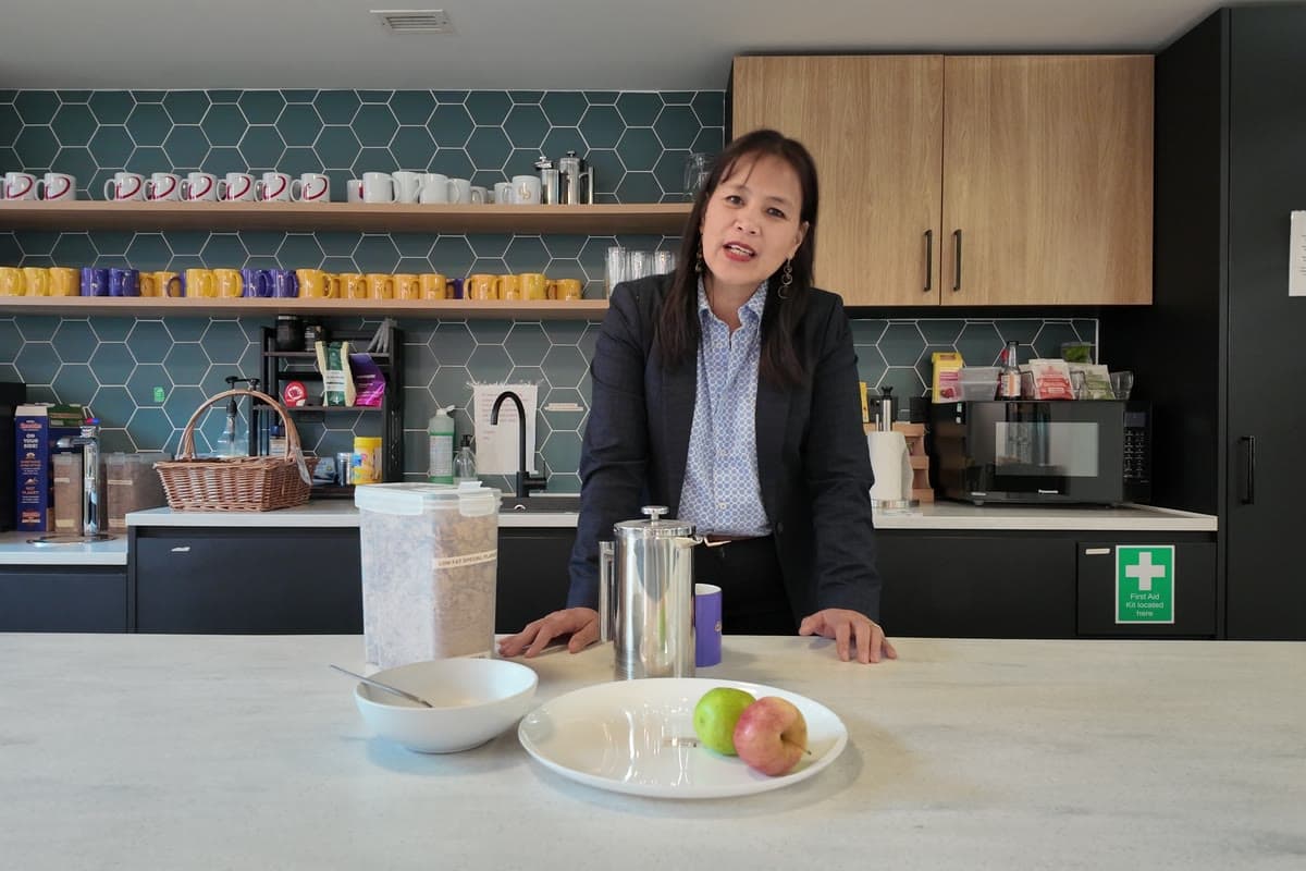 Mel Fisher behind a breakfast counter lined with cups, a cafetière and a bowl of fruit