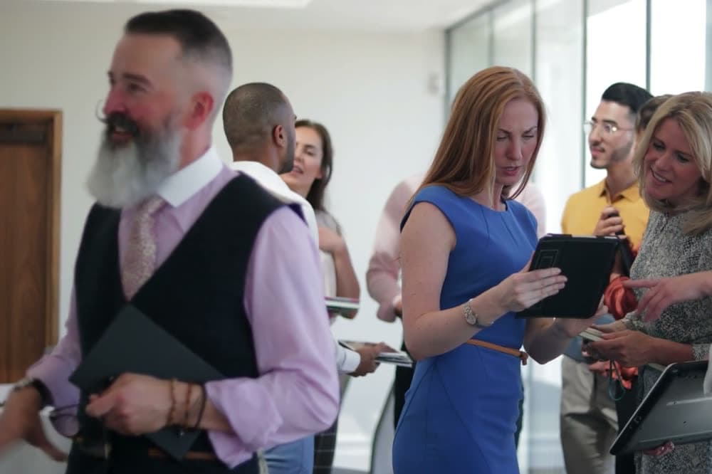 A room of business owners arriving at a morning networking meeting, folders and tablets in hand.