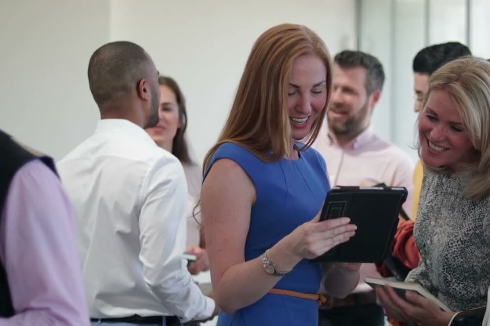 A small group of business owners laughing over a tablet at a networking meeting.