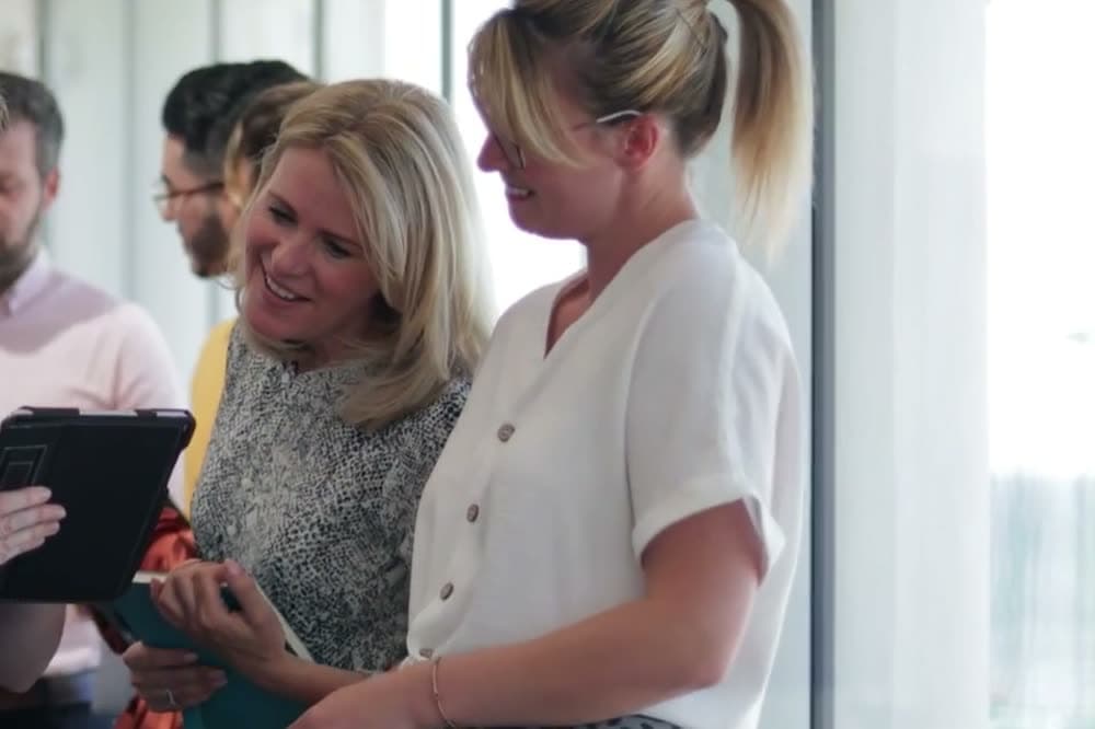 Two women comparing notes on a tablet during a morning networking meeting.
